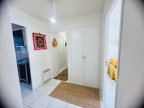 En hall med vita väggar, en takfläkt, en dörr, en liten matta och en gul stol.