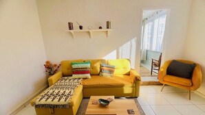 A living room with a yellow sofa, a coffee table, and a chair. There are shelves with decorative items on the wall. - Comfortable apartment near the center - 4 guests (Amélie-les-Bains-Palalda)