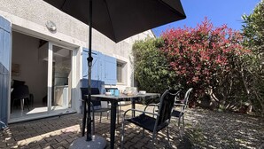Een terras buiten met een tafel, stoelen, een grote parasol en uitzicht op een huis met een schuifdeur.