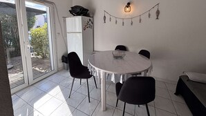 Een eethoek met een ronde tafel, stoelen, een koelkast en een slinger hangende lampjes.