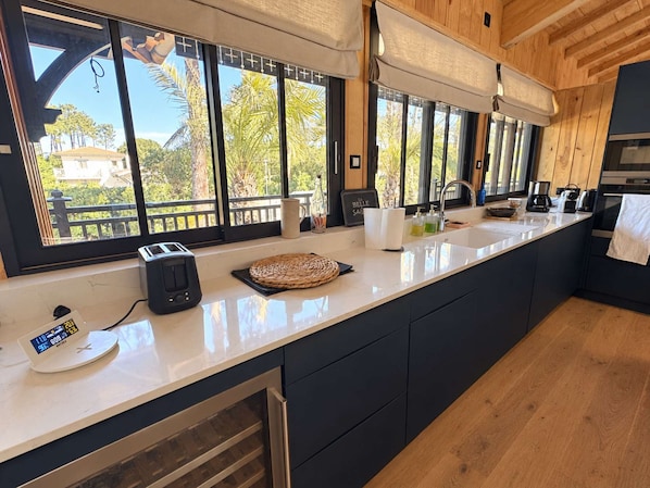 Una cocina moderna con una isla grande, horno empotrado y vistas al exterior a través de amplios ventanales.