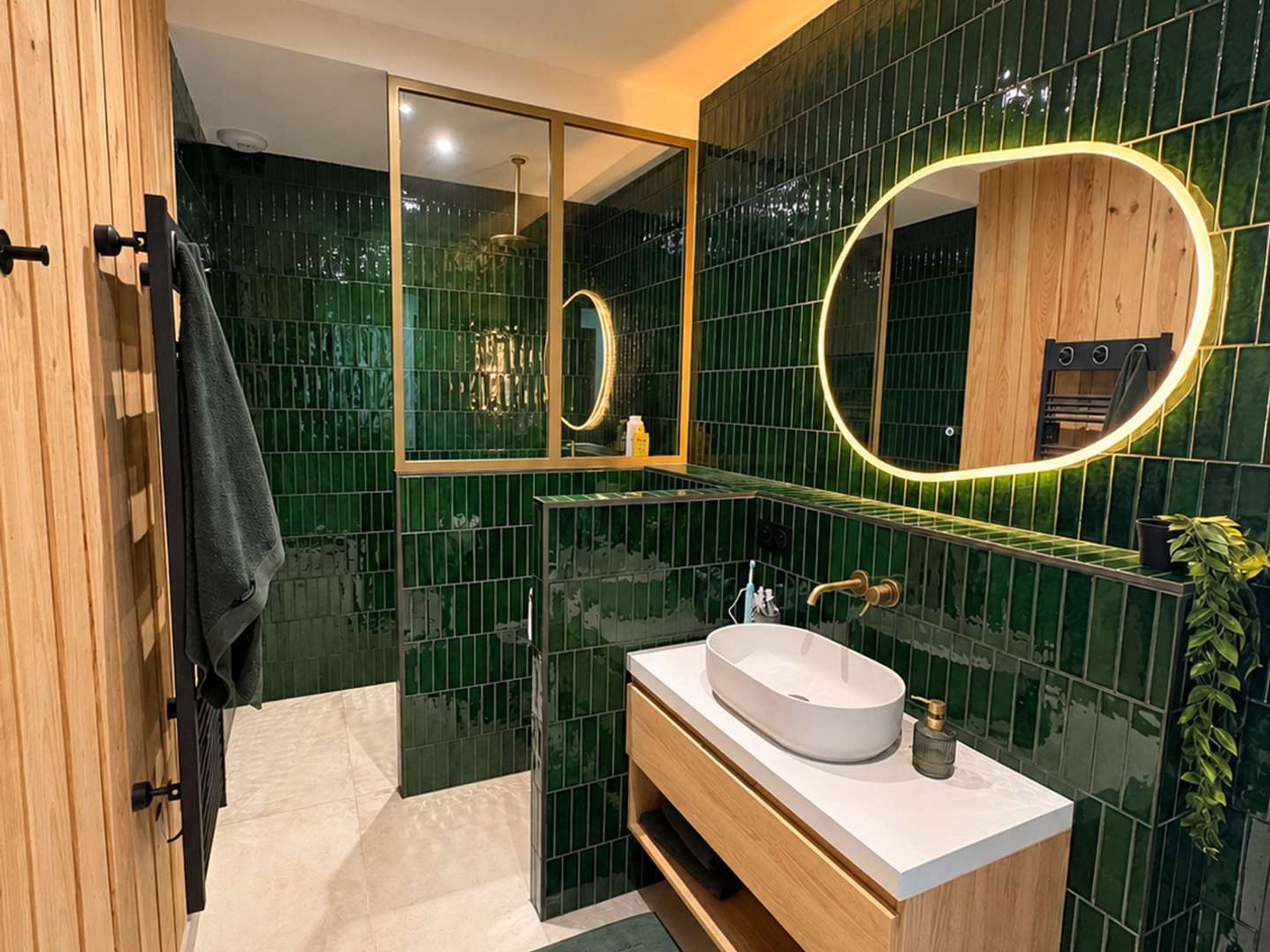 Ein modernes Badezimmer mit einem großen Spiegel, einem weißen Waschbecken und grünen Fliesen.