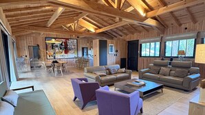 Een ruime woonkamer met houten balken, een eethoek en een groot raam.