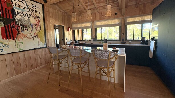 Een houten interieur met een keukenhoek, barstoelen en grote ramen.