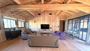 Een ruime woonkamer met een grote televisie, houten wanden en een bank.