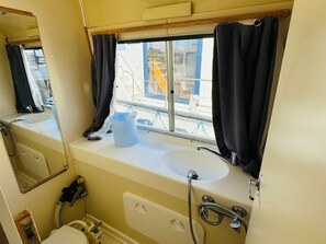 A bathroom with a sink, mirror, and window with curtains. - Secure boat at dock - 6 guests (Colombiers)