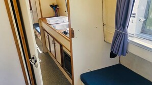 Une petite pièce compacte, équipée d’un lit superposé, d’un lavabo et d’une fenêtre avec des rideaux.