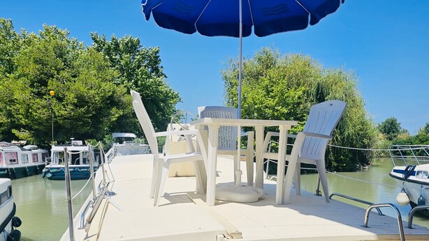 Un bateau doté d’un pont comprenant un coin salon avec un fauteuil blanc, une petite table et un parasol bleu.