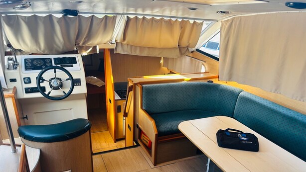 A compact interior with a steering wheel, a small kitchenette, a dining area, and a sleeping berth.