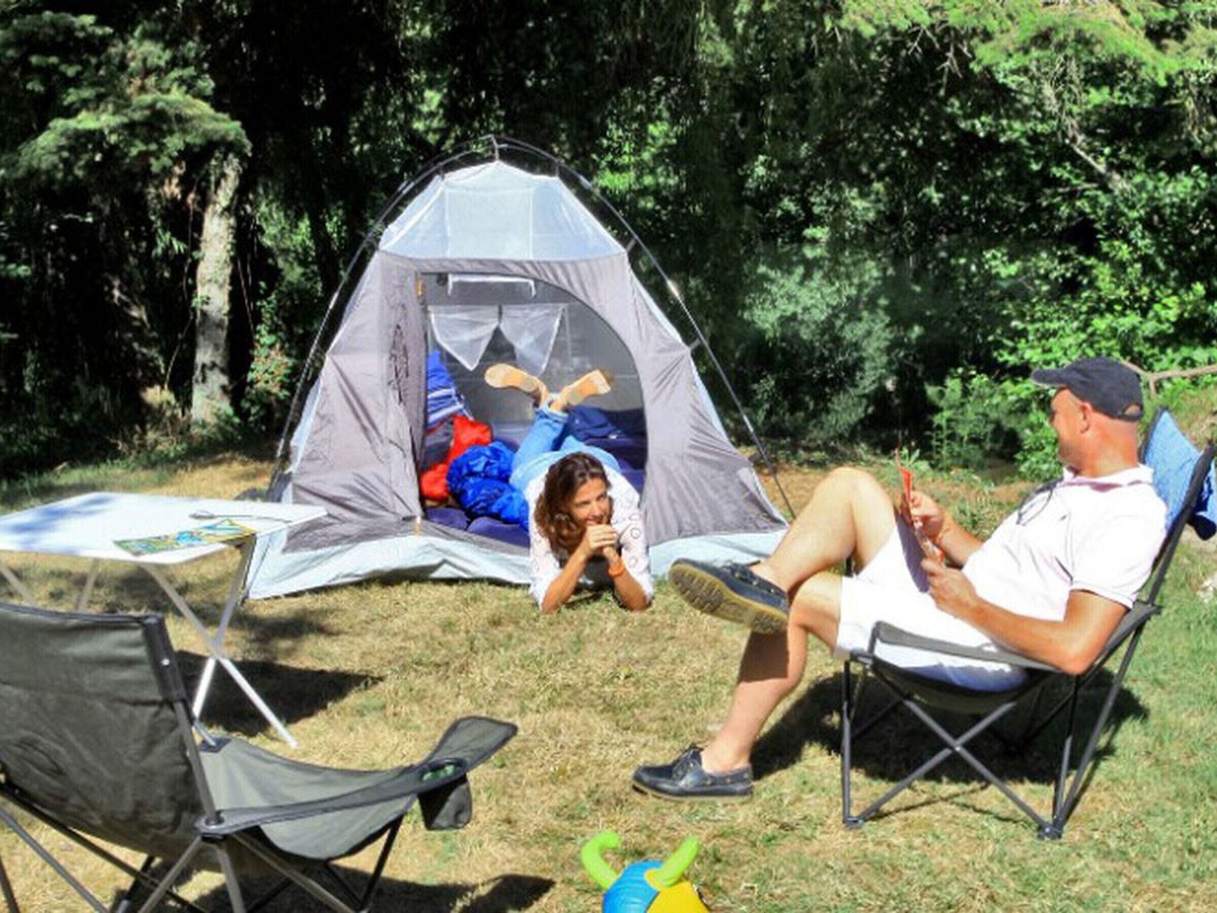 Ein Zelt steht auf einer Wiese, in der Nähe befinden sich ein Tisch und Stühle.