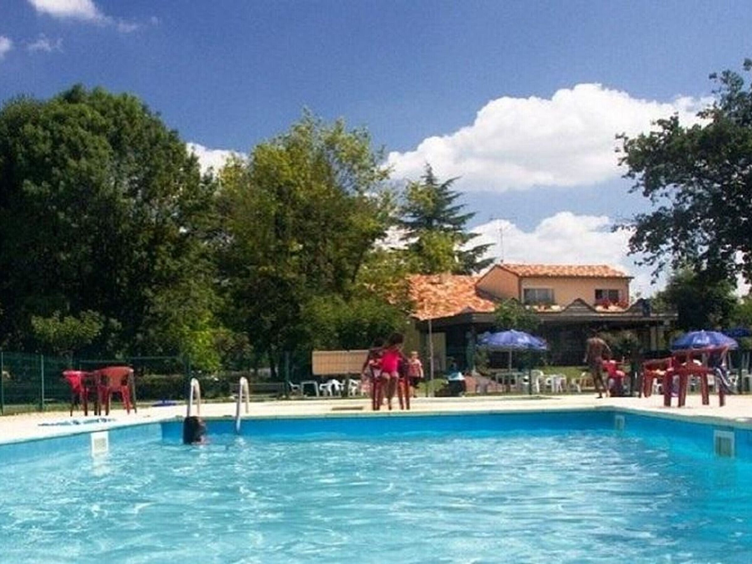 Ein Swimmingpool mit klarem, blauem Wasser, umgeben von Bäumen und einem Gebäude mit einem Ziegeldach.