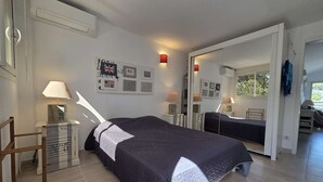 Un dormitorio con una cama, una mesita de noche con lámpara, un espejo y una pared decorada con marcos.
