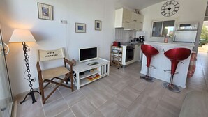 Un espacio habitable pequeño con kitchenette, una zona de comedor con taburetes rojos, televisor y lámpara.