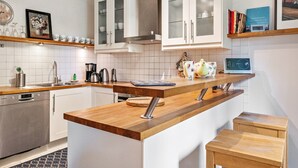A modern kitchen with white cabinets, a wooden countertop, a built-in dishwasher, and a coffee machine.