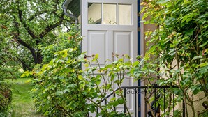 A white door with a window, surrounded by greenery and a metal railing.