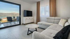 A modern living room with a sofa, a small table, a TV, and a balcony with a view.