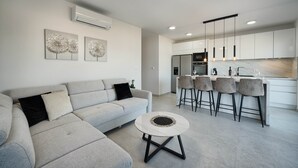A modern living room with a sofa, a coffee table, and a kitchen area with bar stools.