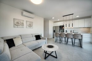 A modern living room with a sofa, a coffee table, and a kitchen area with bar stools.
