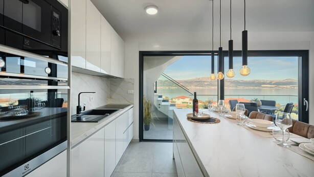 A modern kitchen with a view of a balcony, a dining area with a table set for four, and a large window overlooking a scenic landscape.