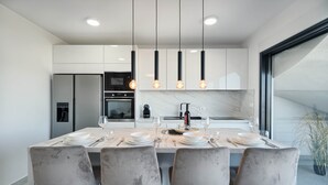 A modern kitchen with a marble countertop, four grey chairs, and pendant lighting.
