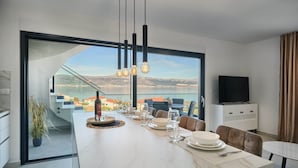 A modern dining area with a large table set for four, a TV, and a view of the mountains.