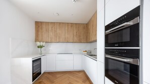 Una cocina moderna con armarios blancos, suelo de madera en espiga y horno empotrado.