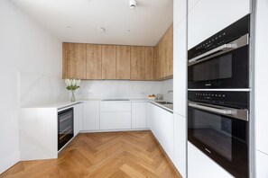 Una cocina moderna con armarios blancos, suelo de madera en espiga y horno empotrado.
