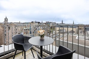 Ein Balkon mit zwei Stühlen und einem Tisch, der einen Blick auf eine Stadt mit Gebäuden und einem Glockenturm bietet.