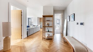Un interior moderno con suelo de madera, un banco, una estantería y un acceso a otra habitación.