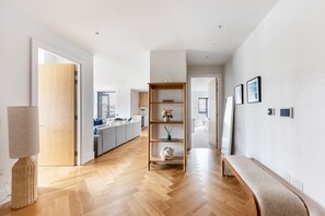 Un interior moderno con suelo de madera, un banco, una estantería y un acceso a otra habitación.