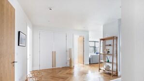 Una habitación amplia con piso de madera, una puerta blanca y una estantería con objetos decorativos.
