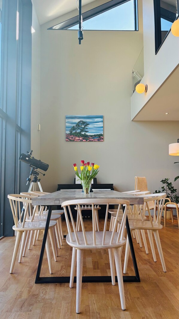 Un coin repas avec une table et des chaises en bois, un télescope, un tableau et un vase de tulipes.
