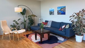 Un salon avec un canapé bleu, une chaise en bois, une table basse et plusieurs plantes en pot.