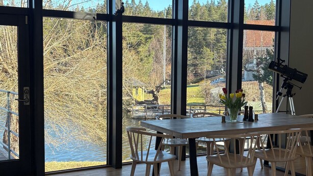 A spacious room with large windows, a wooden table, chairs, a telescope, and a rug. - Waterfront villa with private dock & wood-fired sauna in nature reserve (Saltsjö-Boo)