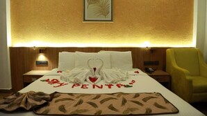 A hotel room with a bed, a framed picture on the wall, a yellow chair, and a heart-shaped towel arrangement on the bed. - SKY PENTA RESIDENCY (Iritty)