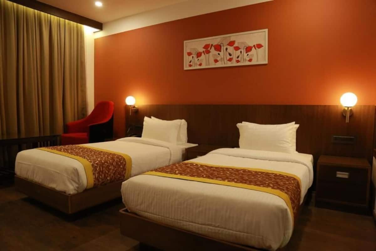 A hotel room with two beds, a red chair, and a painting on the wall.