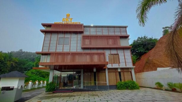 A multi-story building with a modern architectural design, featuring a prominent entrance with glass doors and a covered walkway. - SKY PENTA RESIDENCY (Iritty)