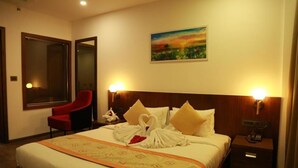 A hotel room with a bed, a red chair, a nightstand, a wall painting, and a mirror. - SKY PENTA RESIDENCY (Iritty)