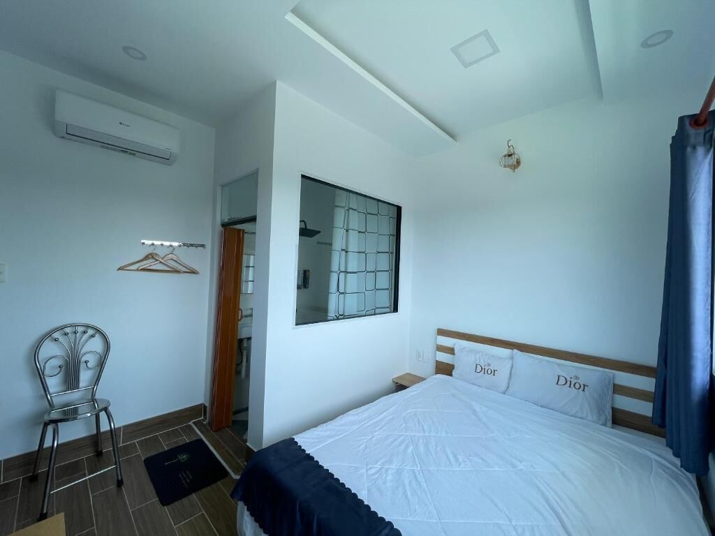 Un dormitorio con cama, una silla, aire acondicionado, una ventana con vistas y una puerta.