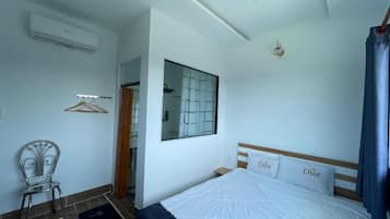 Un dormitorio con cama, una silla, aire acondicionado, una ventana con vistas y una puerta.