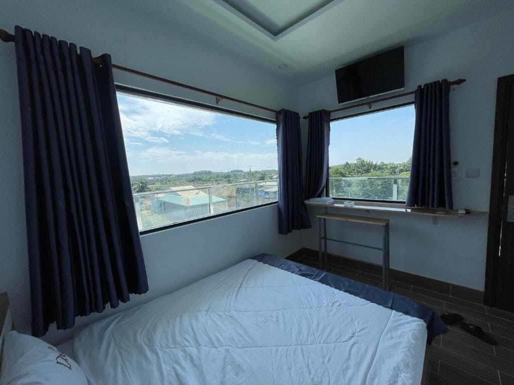 A hotel room with a bed, a desk, a TV, and large windows with curtains.