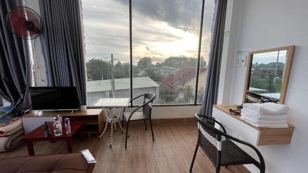 A room with a large window, a TV, a desk, a chair, a sofa, and a mirror. - Ngoc An Hotel (Long Hoa)