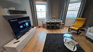 Ein modernes Wohnzimmer mit einem Flachbildfernseher, einem Esstisch mit Stühlen, einem gelben Sessel und einem weißen Sofa.