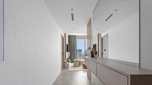 Un couloir d’hôtel moderne avec un parquet en chevrons, un grand miroir et une vue sur le paysage urbain par une fenêtre.