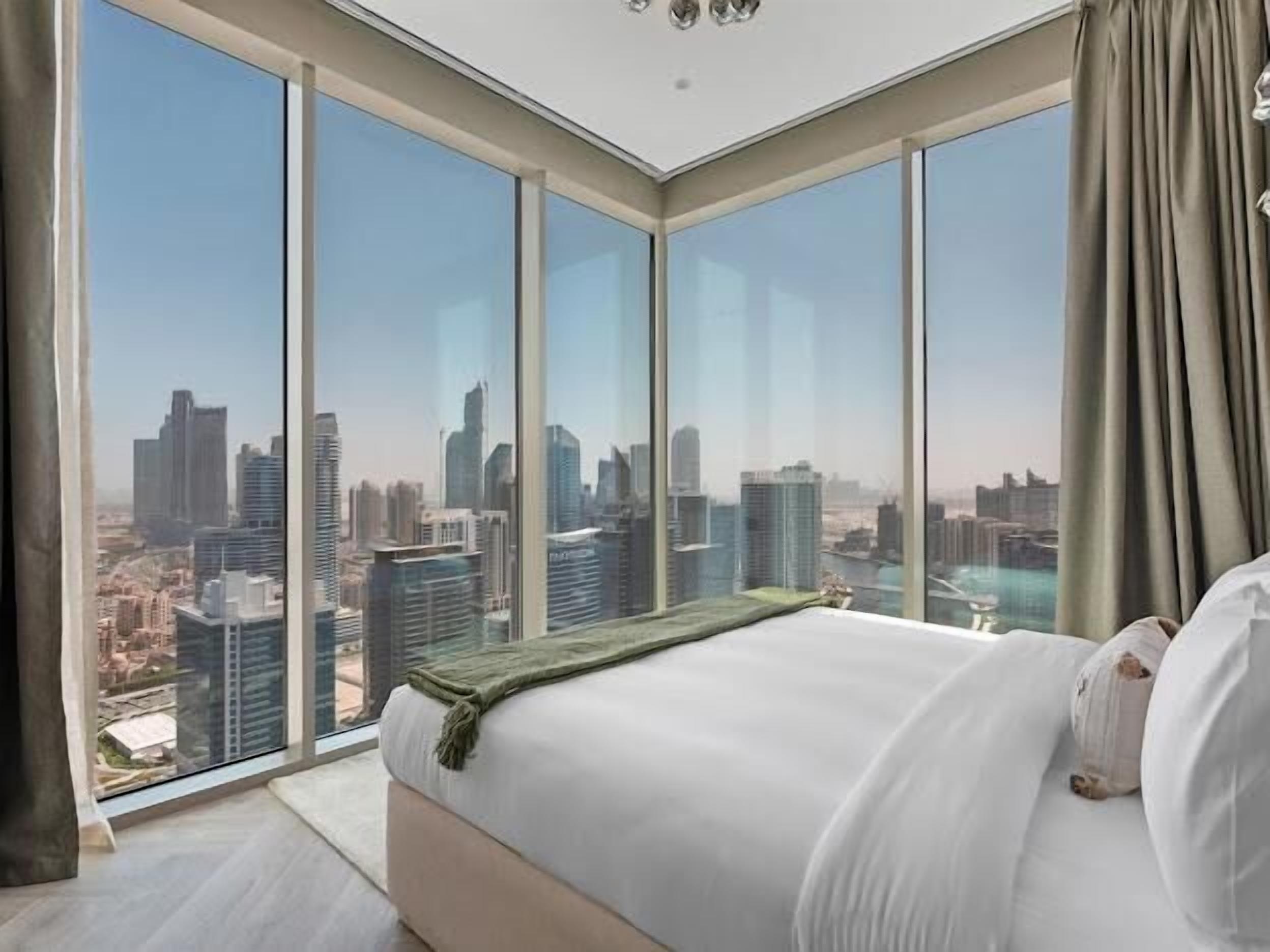 Un dormitorio con una cama grande, vistas a un paisaje urbano a través de ventanales del suelo al techo, y un diseño moderno en el techo.