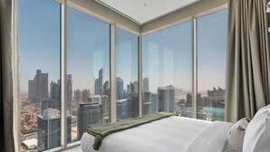 Une chambre dotée d’un grand lit, offrant une vue sur le paysage urbain grâce à de larges fenêtres du sol au plafond, et agrémentée d’un design moderne au niveau du plafond.