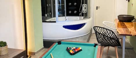 A pool table with balls and cues, a chair, a small table with a bowl, and a door.