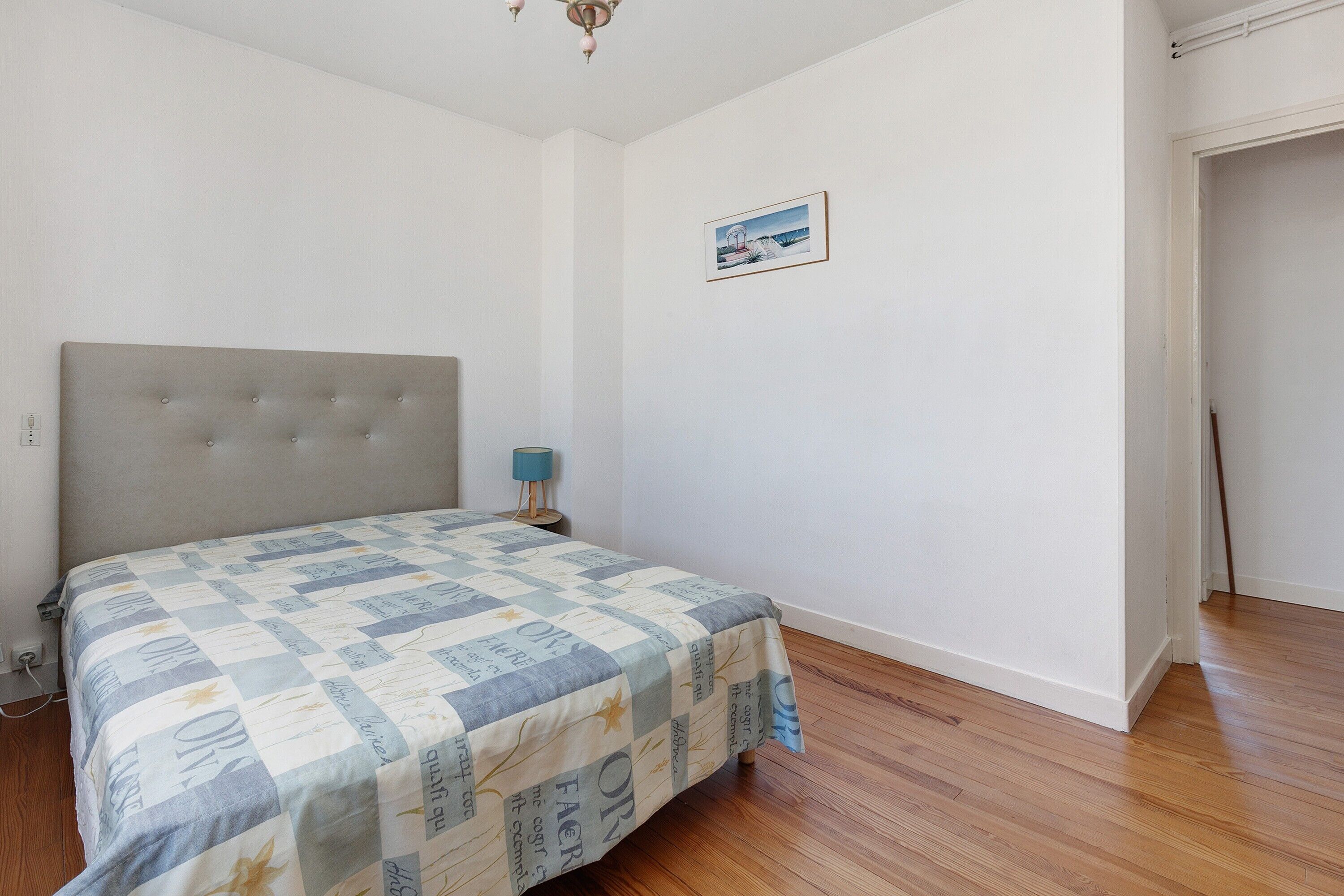 Une chambre à coucher avec un lit, une table de chevet, une lampe et un tableau encadré au mur.