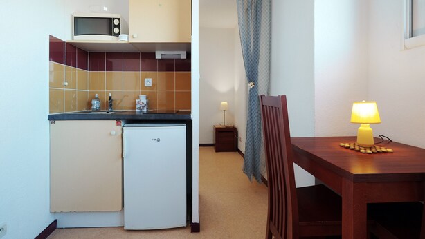 A compact kitchen with a microwave, refrigerator, and a dining area with a table and chair. - Saint Clair Ndeg318 - ST3 (Agde)