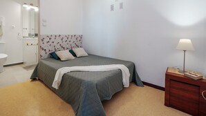 A bedroom with a bed, a bedside table, a lamp, and a bathroom visible in the background. - Saint Clair Ndeg318 - ST3 (Agde)